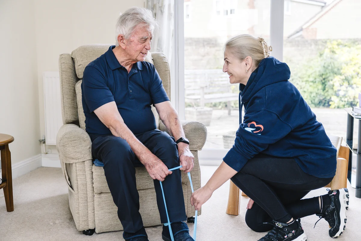 An EverFit coach supporting a seated older man with a resistance-band exercise