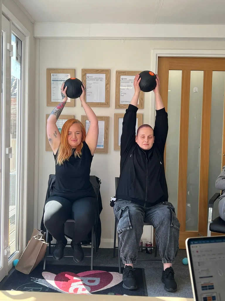 Two training participants practising seated overhead lifts with exercise balls